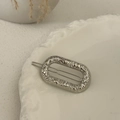 Close-up of a silver hammered metal oval hair clip on a white decorative ceramic plate - Silver-Oval
