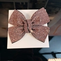 Detail of pink rhinestone bow hair clip with sparkling crystal inlay on white stand - Purple