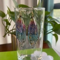 Detailed shot of gradient wing earrings with gold foil hanging on a clear glass rim - Rainbow Gold Foil