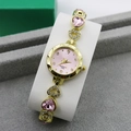 Detailed close-up of a gold quartz watch with pink heart crystals on a velvet display - Gold + Pink