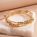 Detail eines mehrlagigen Goldarmbands mit glitzernden Steinchen auf einem Steinsockel - Gold