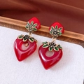 Detail of red heart strawberry earrings with golden floral accents on white linen - Strawberry Heart Style / Red