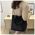 Modern black nylon tote bag shown on model with a beige knit sweater in a cozy room - Black