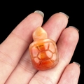 Handcarved carnelian tortoise figurine with detailed shell texture in a hand - Colored Jade