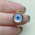 Detailed close-up of a gold-rimmed evil eye charm with blue details and mother of pearl - Gold
