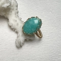 Macro shot of handmade wire-wrapped gold ring with oval turquoise stone on white coral - Amazonite