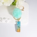 Mint green pompom keychain with blue resin alphabet pendant and gold foil detailing - Letter I