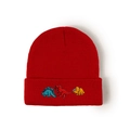 Close-up of red knitted kids beanie with colorful embroidered cartoon dinosaurs - Kids (50-53cm) / Red