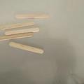 Natural light wood popsicle sticks scattered on a grey surface for DIY craft projects - 100 Pcs/Pack