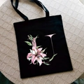 Black canvas tote bag featuring a pink lily and letter U print on a minimalist surface - Letter U / Black