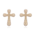 Gros plan de boucles d'oreilles croix dorées avec perles d'imitation sur fond blanc - Style Croix (Boucles d'oreilles) / Doré