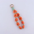 Macro detail of hand-woven daisy keychain with orange petals and golden metal clasp - Orange Red
