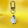 Dettaglio di portachiavi a pinguino 3D in resina con clip in metallo su sfondo giallo - Pinguino con le mani abbassate