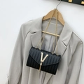 Fashionable black woven crossbody bag with gold V-logo and fringe on a gray blazer - Black