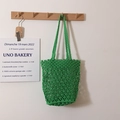 Bolso tote de ganchillo verde vibrante con patrones huecos colgado en un soporte - Verde