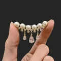 Dettaglio di spilla dorata con eleganti perle bianche e pietre di zircone pendenti - X0260 Zircone Nappina