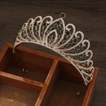 Baroque gold crown with green gems and rhinestones displayed on a rustic wooden box - Gold Green Zirconia