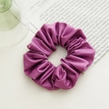 Detail shot of purple satin scrunchie with glossy texture and rich pleats on white desk - Basic Style / Purple