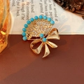 Primer plano detallado de un broche vintage dorado en forma de abanico con cuentas azules - Dorado-Azul