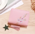 Pink zippered mini wallet with floral embroidery and tassel charm on wood surface - Light Pink