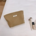 Detail of khaki waffle weave toiletry bag with zipper and simple wish label on bed - Light Camel