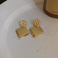Detail of geometric square gold metal earrings on a white ceramic plate - Gold