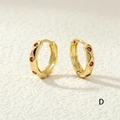 Makroaufnahme goldener Creolen mit gewelltem Design und roten Zirkonia-Steinen - Rosaroter Zirkon / Rosarot