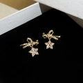 Dettaglio orecchini a fiocco dorati con stelle in zircone su velluto nero da gioielleria - Orecchini Pendenti con Fiocco e Pentagramma / Oro
