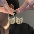 Dettaglio di orecchini a nappa dorati con strass scintillanti tenuti da un modello - R2567 Nappa dorata