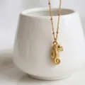 Vue macro d'un pendentif hippocampe doré avec texture fine sur une chaîne perlée - Hippocampe Doré