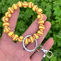Hand holding a yellow softball beaded keychain wristlet with silver metal hardware detail - Yellow Baseball