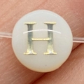 Gros plan d'une perle en nacre blanche avec lettre H dorée pour bijoux DIY - Lettre H