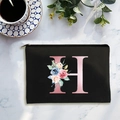 Black canvas cosmetic bag with floral letter H print on white marble surface - Letter H