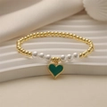 Elegantes Goldperlenarmband mit weißen Perlen und grünem Herzanhänger auf gewellter Basis - Grünes Herz