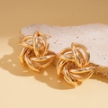 Macro view of gold geometric intertwined swirl earrings on a textured stone surface - Gold