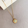 Detalle de colgante de sol vintage dorado con gema verde sobre fondo texturizado - Collar de Acero de Titanio Sunburst Verde Claro