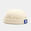 Detailansicht der beigen Cord-Docker-Mütze mit feiner Textur und blauem Logo-Etikett - Verstellbar / Beige