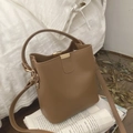Chic brown leather bucket bag with top handle and gold hardware on vintage newspaper - Brown