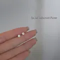Close-up of minimalist 925 silver mini hollow flower stud earrings held by hand - HyunA Floral / Silver