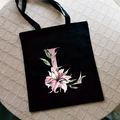 Black canvas tote bag featuring pink Lily Letter print and floral pattern on a stool - Letter L / Black