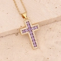 Macro view of golden cross pendant with purple center stone and white zircon accents - Purple