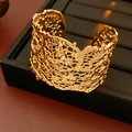 Dettaglio di un ampio bracciale dorato con texture lavica irregolare su scatola nera - Bracciale-Oro / Oro