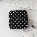 Flat lay of a quilted black cosmetic bag with white heart patterns on a white desktop - White Heart