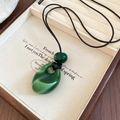 Close-up of green teardrop acrylic pendant on black cord over a beige wooden jewelry tray - Dark Green