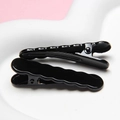 Close-up of black wave-shaped hair clips with glossy finish on a white plate - Black