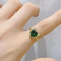 Nahaufnahme eines vergoldeten Herzrings mit grünem Edelstein an einem Finger im Licht - Grünes Herz Stein Stil (E)