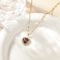 Detailed view of heart-shaped necklace with red gemstone and pavé zircon on white plate - December - Medium Purple