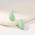 Macro detail of mint green teardrop stud earrings on a textured white stone surface - Cyan