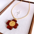 Dettaglio di un ciondolo floreale vintage in resina marrone e oro su lino bianco - Marrone oro
