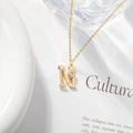 Detailed shot of golden M initial necklace with zircon flower pendant on aesthetic background - Letter M